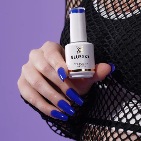 Hand holding a nail polish brush over a jar of BlueSky Builder Gel on a pink background